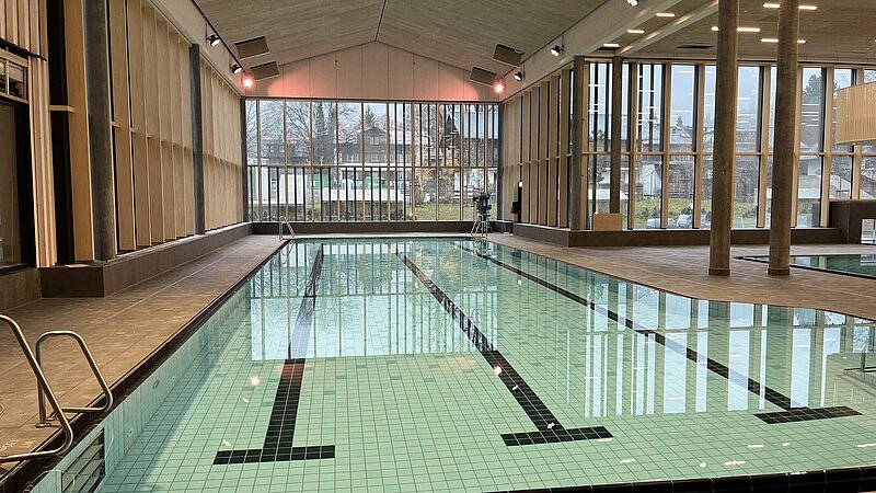 Innenansicht eines Schwimmbeckens der Therme in Oberstdorf mit großem Glasfenster im Hintergrund.
